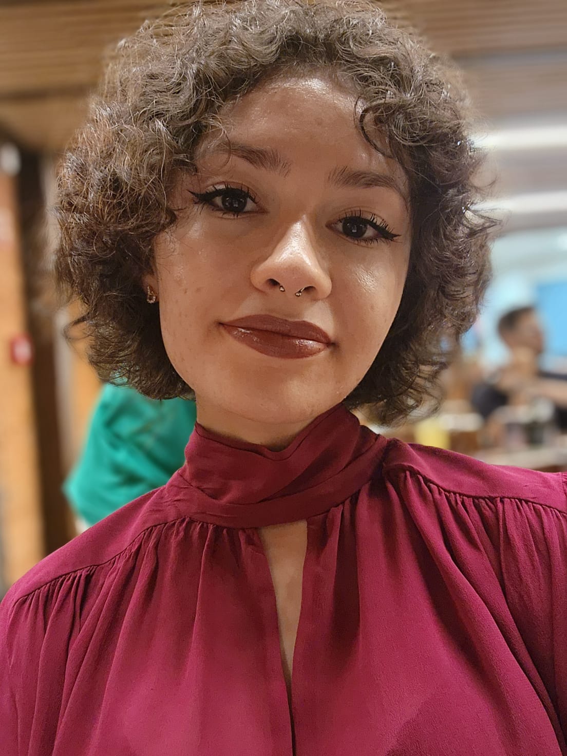 imagem da brunna, mulher branca, de cabelos cacheados, castanhos e curtos, vestindo uma blusa de gola alta da cor marsala